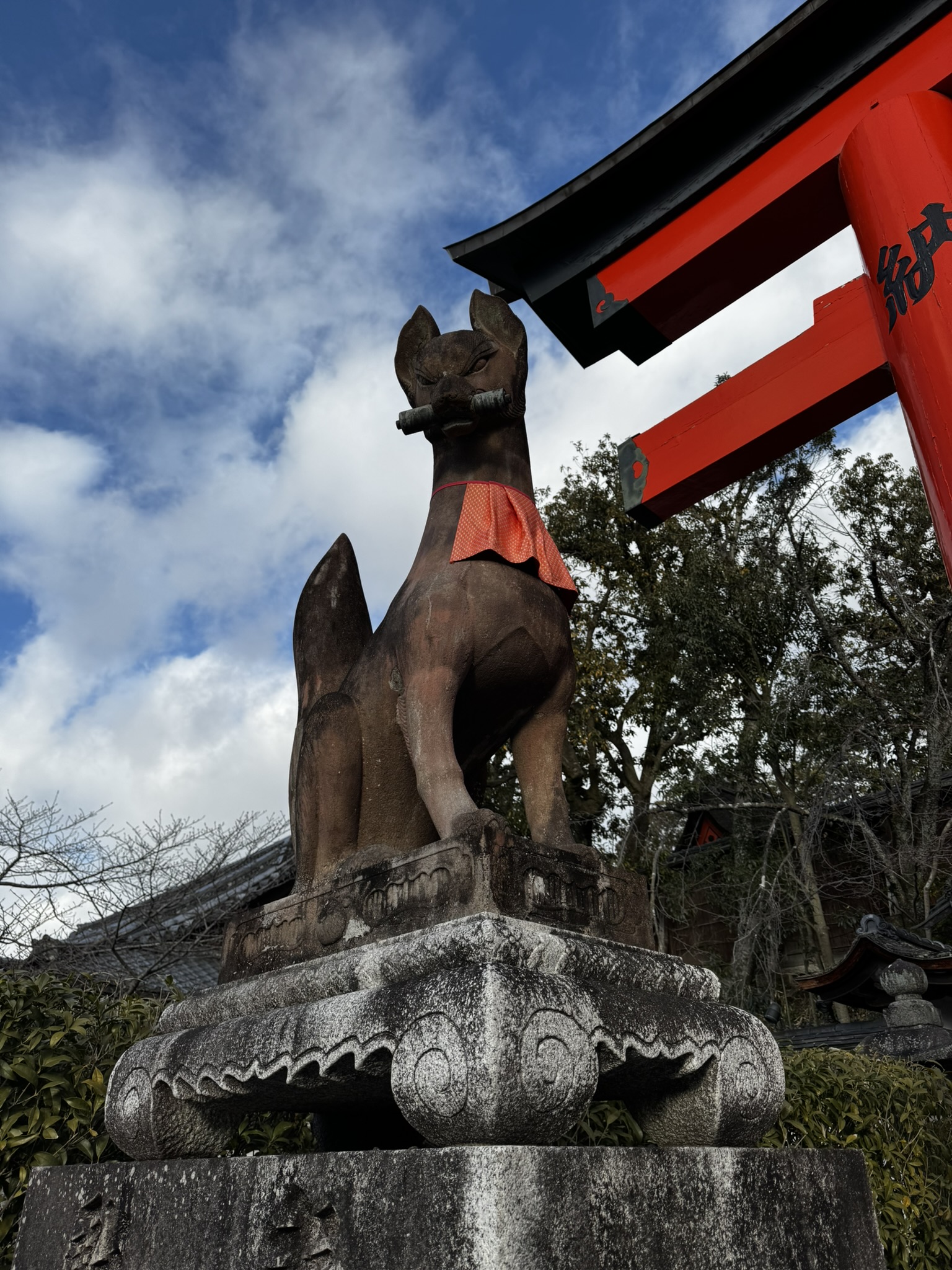 Fox statue beside a red shrine gate at Fushimi Inari