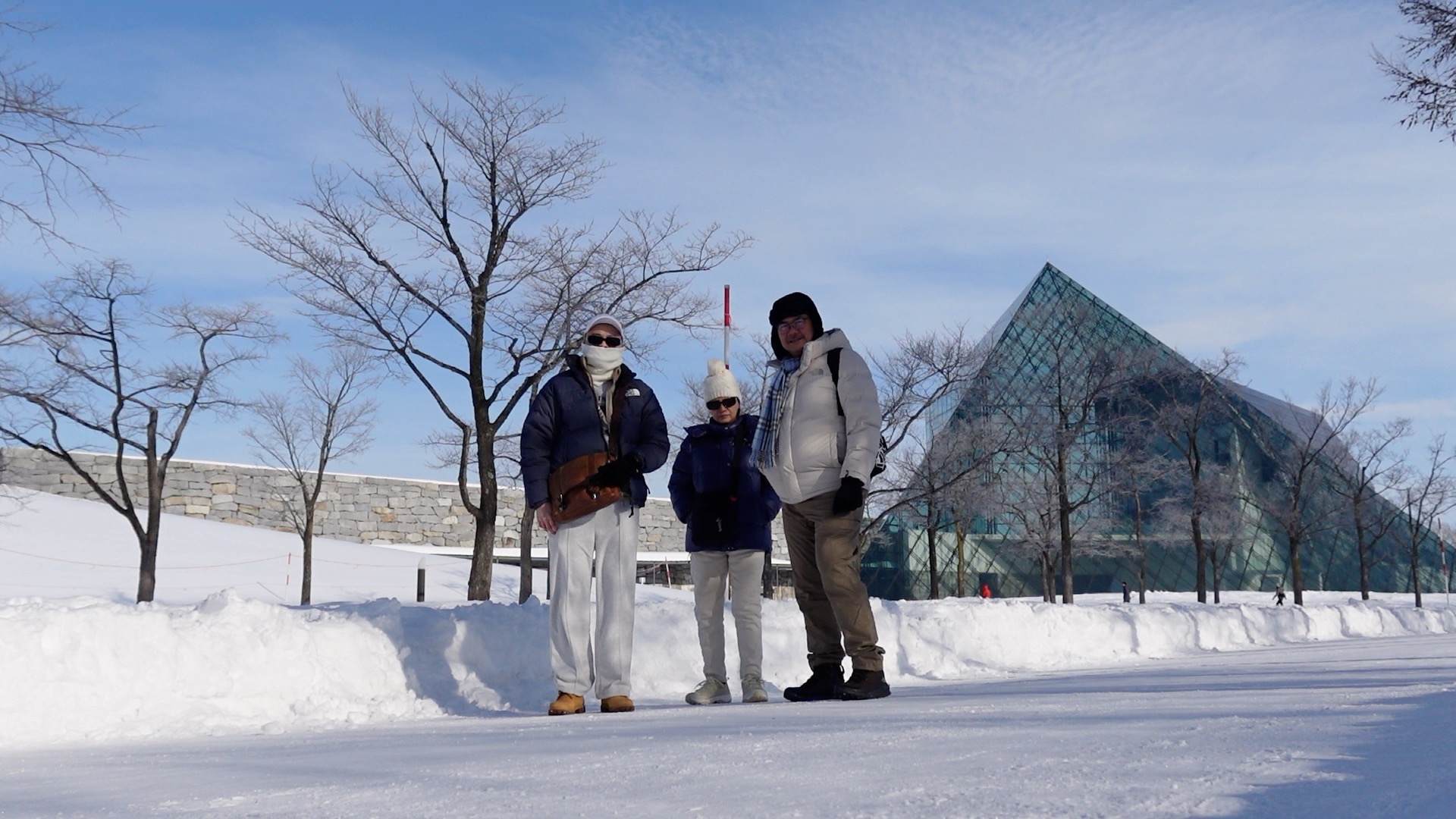 Family standing in the snow with Moerenuma Park glass pyramid behind them