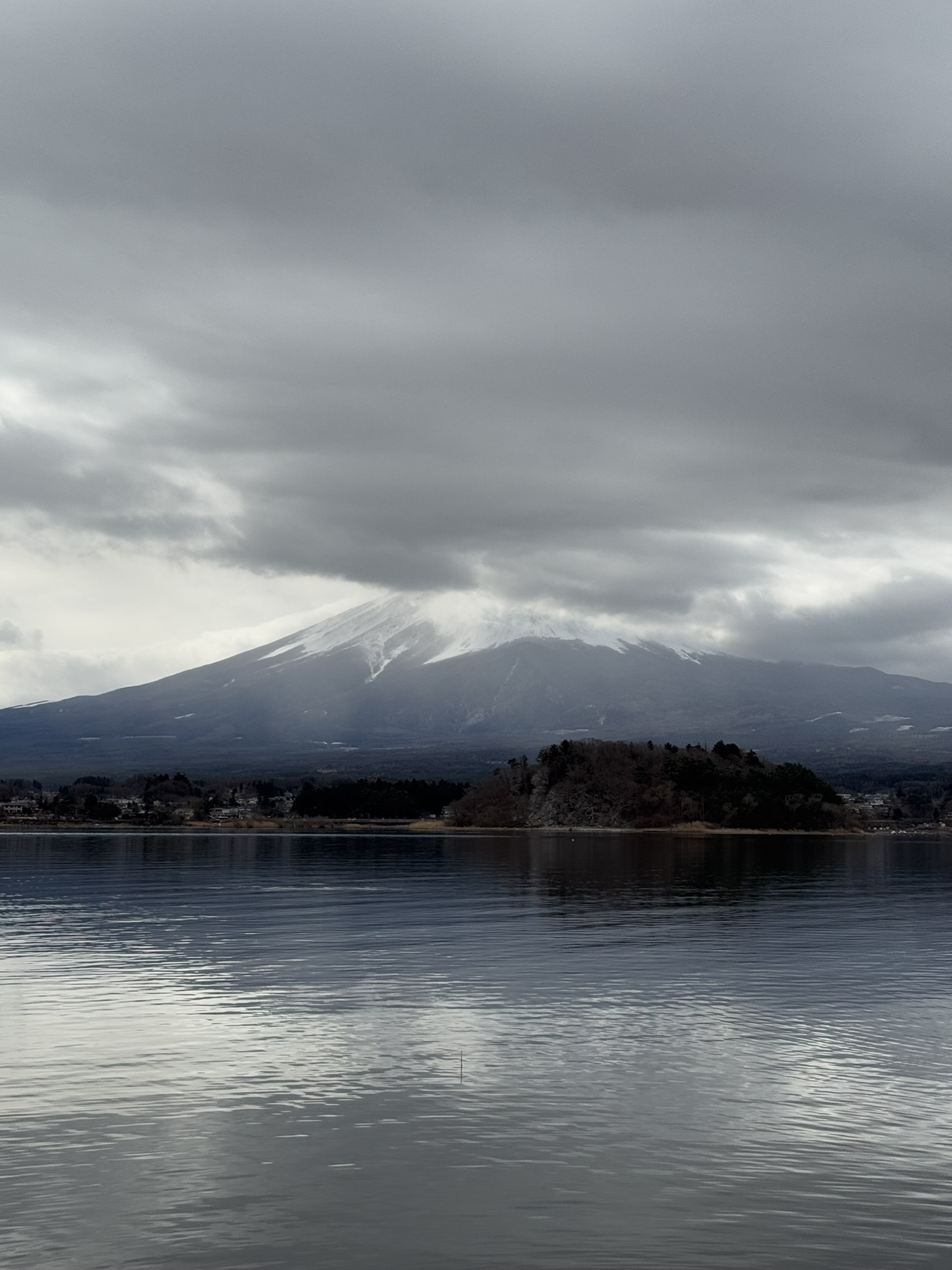 Mt. Fuji partly covered by clouds over a calm lake
